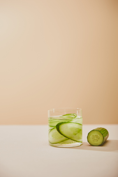 Glass of water with sliced cucumbers on table isolated on beige  - Foto, Bild