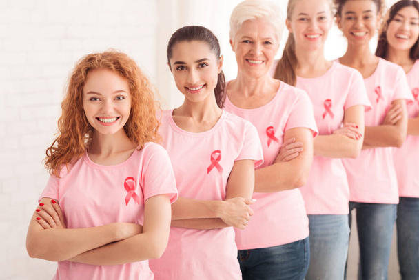 ピンクの意識を持つボランティアTシャツが白い背景に一緒に立っている - 写真・画像