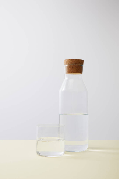 Bottle with cork and glass filled with water on isolated on grey - 写真・画像