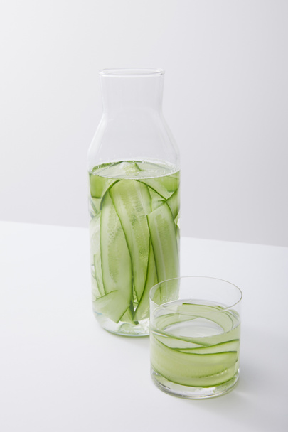 high angle view of bottle and glass with water and sliced cucumbers isolated on grey - Foto, immagini