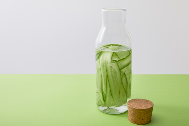 Cork and bottle with water and sliced cucumbers isolated on grey - Fotografie, Obrázek