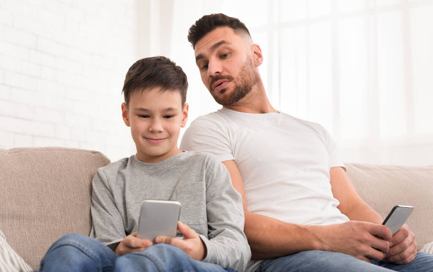 Neugieriger Papa blickt zu Hause auf das Smartphone seines Sohnes - Foto, Bild