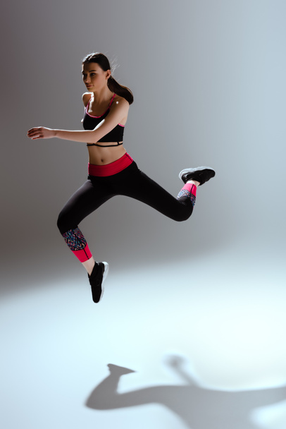 attractive girl in sportswear jumping on grey  - Foto, imagen