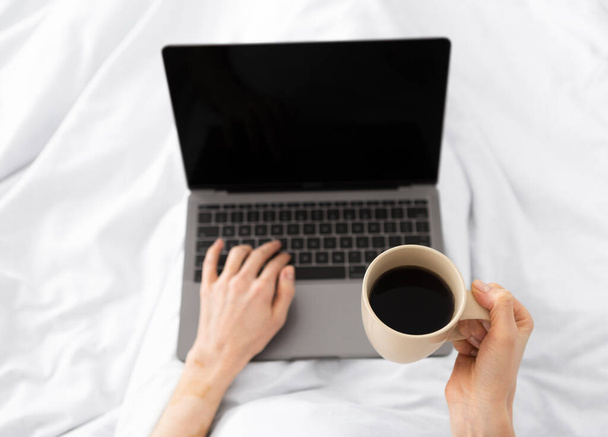 Handen typen op laptop in de ochtend op een wit kussenbed - Foto, afbeelding