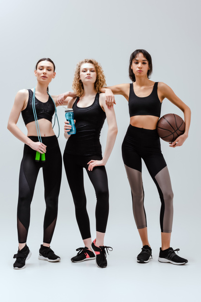 sportive and multicultural girls standing with sport equipment on white  - Foto, Bild