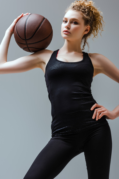 giovane donna in abbigliamento sportivo in possesso di basket e in piedi con mano sul fianco isolato su grigio
 - Foto, immagini