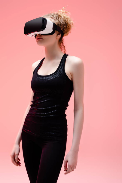sportive woman in in sportswear and virtual reality headset on pink  - Фото, изображение