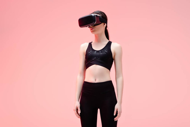 young sportswoman in virtual reality headset standing on pink   - Fotó, kép