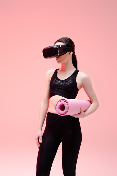 sportswoman in virtual reality headset holding fitness mat on pink   - Foto, immagini