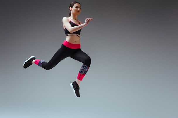 ładna kobieta w odzieży sportowej skacze na szarości - Zdjęcie, obraz