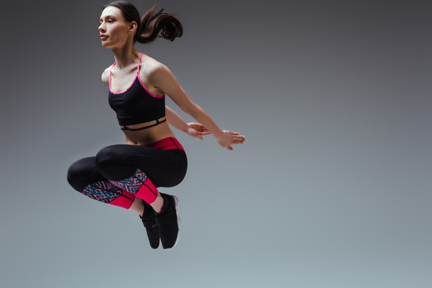 sportive woman in sportswear jumping on grey - Фото, зображення