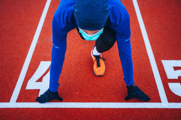Runner wearing medical mask, Coronavirus pandemic Covid-19 in Europe. Sport, Active life in quarantine surgical sterilizing face mask protection. Outdoor run on athletics track in Corona Outbreak - Photo, Image
