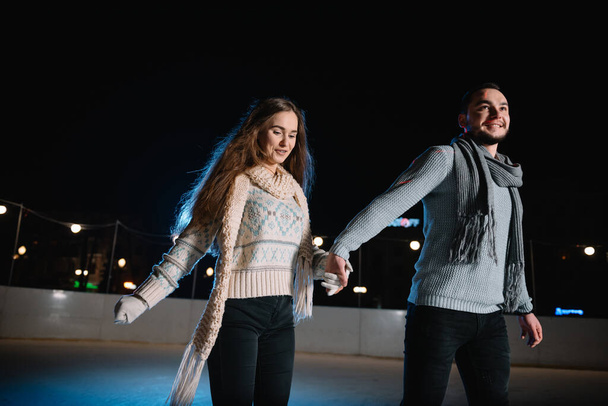 Winter skates, loving couple holding hands and rolling on rink. Illumination in background, night. Concept training. - Fotoğraf, Görsel