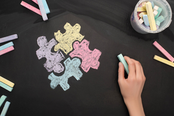 vue du dessus de la femme tenant de la craie turquoise à bord avec dessin puzzle pour la Journée mondiale de sensibilisation à l'autisme
 - Photo, image