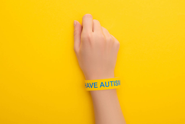 πάνω όψη της γυναίκας χέρι σε βραχιόλι με την επιγραφή του αυτισμού στο κίτρινο - Φωτογραφία, εικόνα