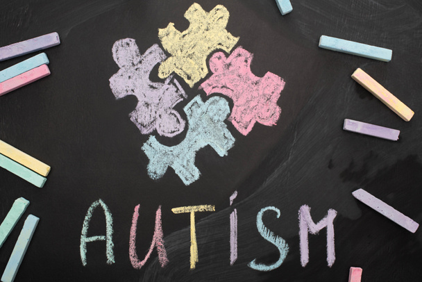 bovenaanzicht van krijt aan boord met woord autisme en puzzeltekening - Foto, afbeelding