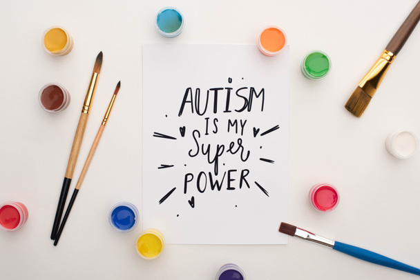 Draufsicht auf Farben, Pinsel und Karte mit Autismus ist mein Superpower-Schriftzug auf Weiß - Foto, Bild