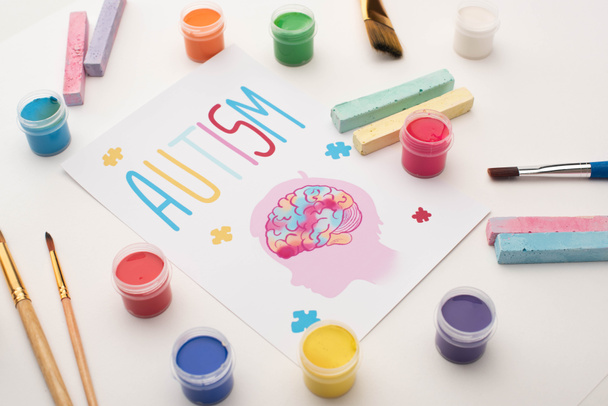 scheda con parola autistica e pittura della testa con cervello e puzzle su bianco con pennelli, gessetti e vernici
 - Foto, immagini
