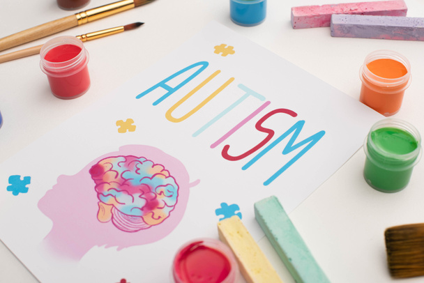 карточка со словом аутизма и рисунок головы с мозгом на белом с кисточками, мелом и красками
 - Фото, изображение