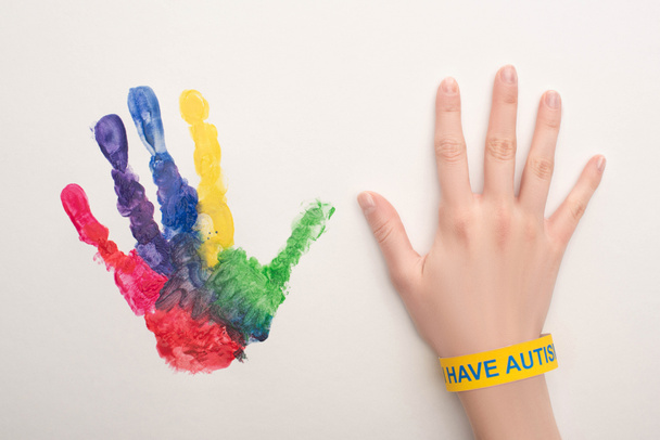 cropped view of female hand with autism bracelet on white with colorful handprint - Photo, Image