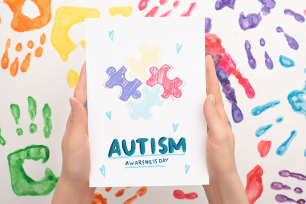 vista recortada de la mujer que sostiene la tarjeta con Autism Awareness Day letras y rompecabezas en blanco con impresiones de mano
 - Foto, imagen