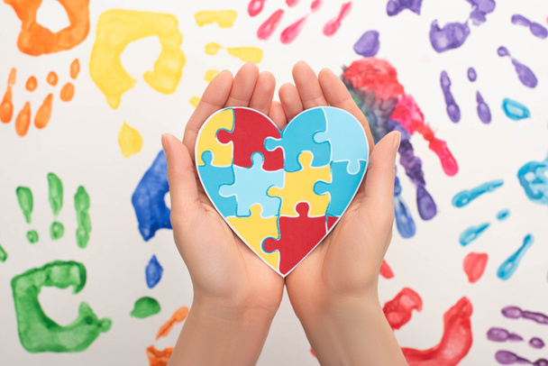 cropped view of woman holding heart with puzzle on white with hand prints for World Autism Awareness Day - Photo, Image