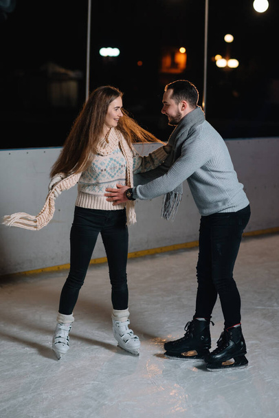 Winter skates, loving couple holding hands and rolling on rink. Illumination in background, night. Concept training. - Zdjęcie, obraz
