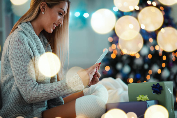 Mignon jeune femme souriante en utilisant la tablette et sourire heureux pendant les vacances confortables de Noël à la maison
. - Photo, image