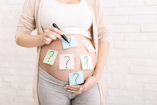 Kobieta w ciąży obejmująca brzuch znakiem zapytania. - Zdjęcie, obraz