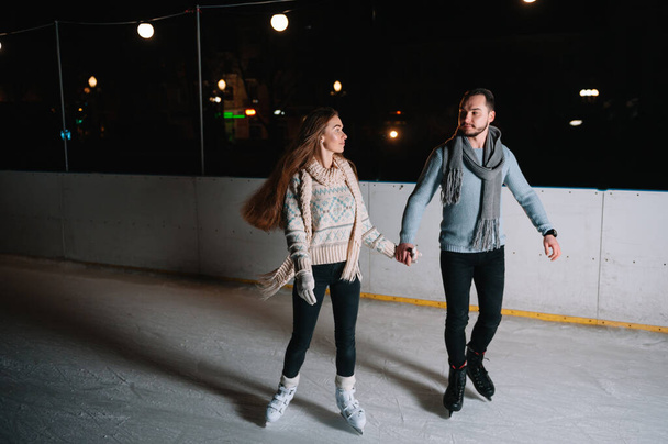 Winter skates, loving couple holding hands and rolling on rink. Illumination in background, night. Concept training. - Photo, Image