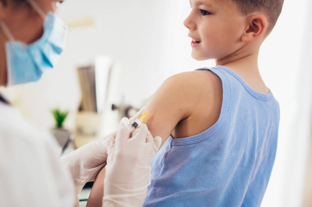 Pediatrician makes vaccination to small boy. Female doctor vaccinating little boy. - Photo, Image