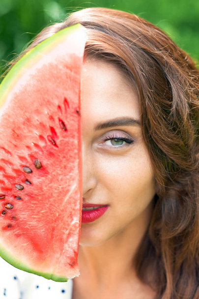 Close up portrait of a girl is holding watermelon slice covering part of face. Woman is holding slice of summertime fruit. - Фото, изображение