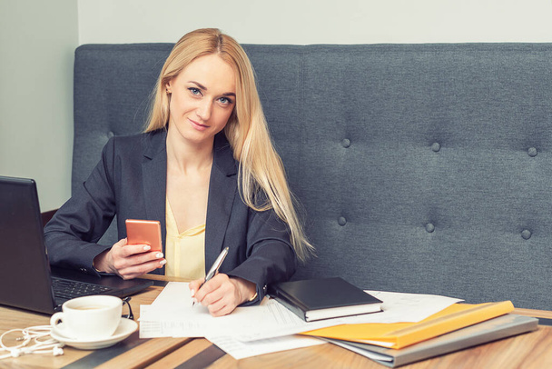 деловая женщина держит смартфон и пишет на пустом месте в офисе, красивая молодая деловая женщина работает на рабочем месте
 - Фото, изображение