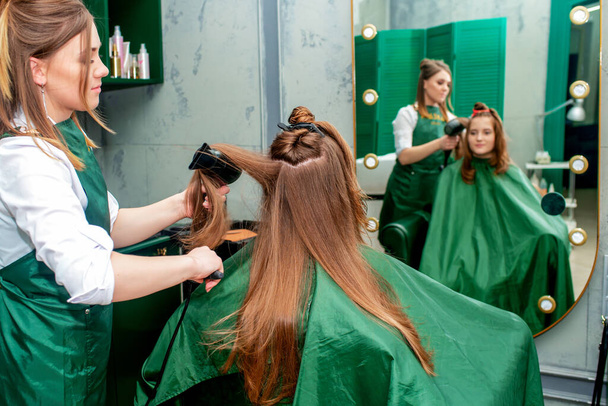 Peluquería hace peinado mientras se seca el cabello de la mujer en el salón de belleza
. - Foto, Imagen