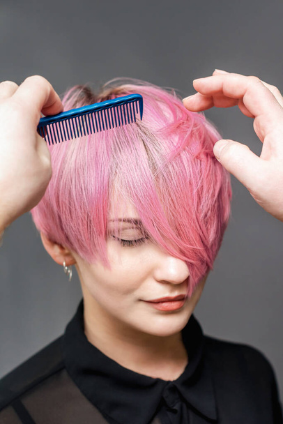 Les mains de coiffeur peignent les cheveux roses courts de la femme sur fond gris gros plan
. - Photo, image