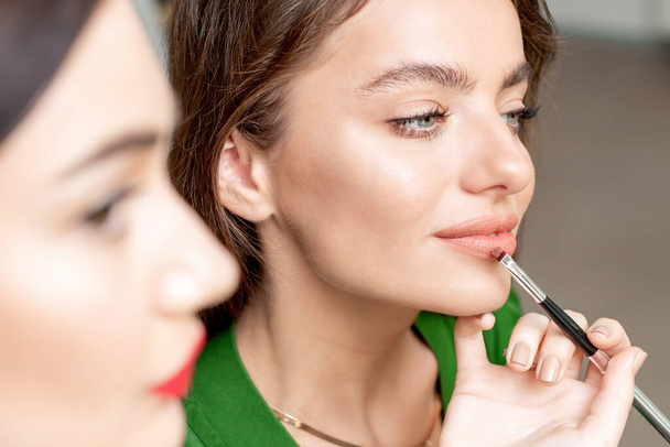 Makeup artist applica il rossetto sul viso della bella donna, il trucco nel processo
. - Foto, immagini