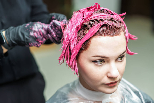 Hairdresser's hands are applying pink color to customer's hair. Hair coloring in a beauty salon. Beauty and people concept. - Photo, Image