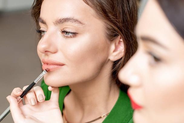Maquillaje artista aplica lápiz labial en la cara de la mujer hermosa, maquillaje en proceso
. - Foto, Imagen