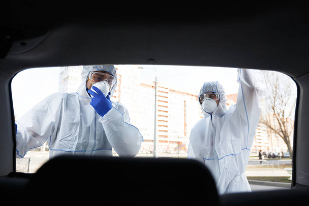 Медичний працівник у захисному костюмі вірусу відкритий багажник і дивиться
 - Фото, зображення