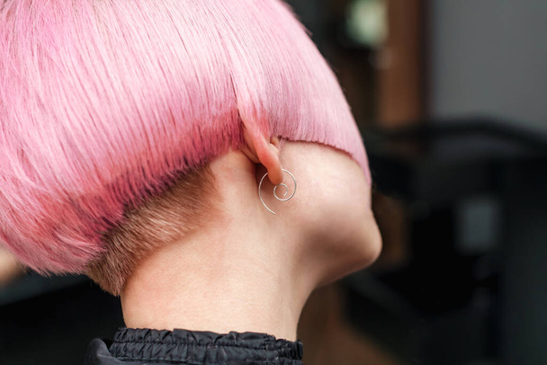 Női rövid hajvágás rózsaszín hajszín közeli oldalnézetben. Női rövid trendi frizura. - Fotó, kép