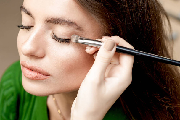 Make-up malíř aplikuje oční stíny prášek s štětcem pro mladou ženu. - Fotografie, Obrázek