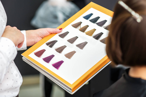 Stylist's hand holding palette of hair dye samples in beauty salon, close up. - Photo, Image