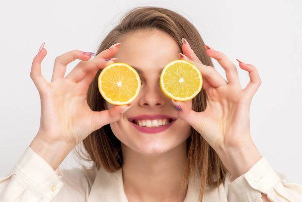 Smiling woman covering eyes with halves of fresh ripe orange fruit, close up. - Fotó, kép