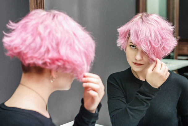 Rózsaszín hajú nő, rövid hajjal a tükröt nézi. Szépségkoncepció. - Fotó, kép