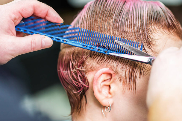 Крупним планом перукаря є різання мокрого рожевого волосся клієнта в салоні. Зачіска вирізає жіноче волосся. Вид збоку рук ріже волосся ножицями
. - Фото, зображення