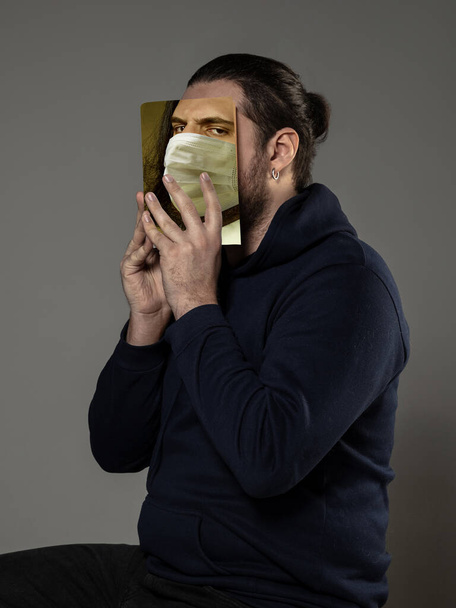 Be safe and read to become someone else - man covering face with book in face mask while reading on grey background - Photo, image