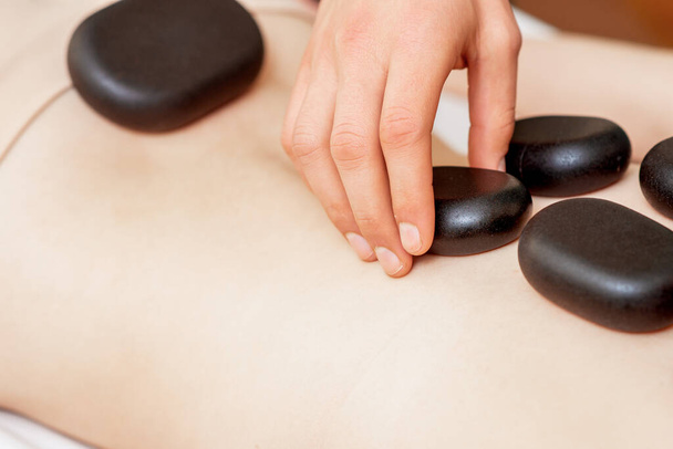 Back massage on back of woman with black hot stones close up. - Φωτογραφία, εικόνα