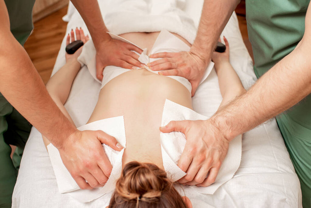 Woman receiving back massage in four hands by two male therapists, close up. - Photo, Image