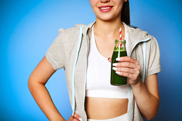 Crop delighted young woman with green smoothie laughing against wall background - Photo, Image