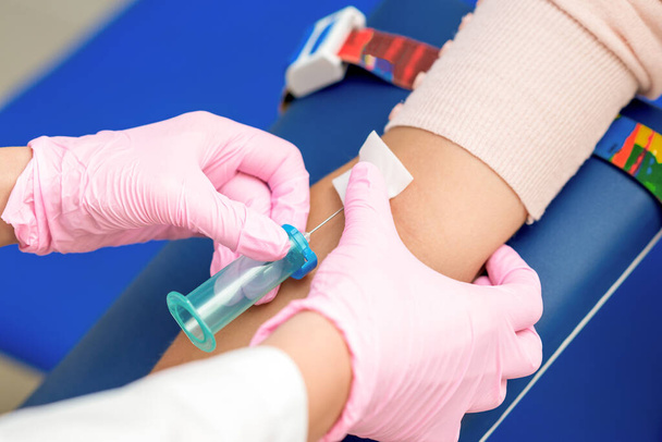 Nurse takes blood sampling introducing a needle into a vein of woman's arm. - Photo, Image